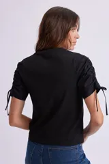 Remera negra de manga corta con cuello redondo y fruncidos ajustables mediante cordones en las mangas.