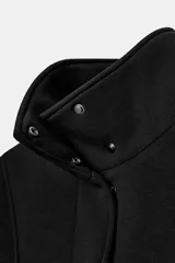 Chaqueta negra de manga larga con cuello subido, bolsillos delanteros y cierre frontal con botones ocultos bajo solapa.