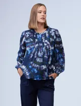 Blusa de gasa estampada con diseño circular en tonos azules, violetas y verde. Delantero plisado, puños elastizados, espalda con abertura ojal y botón.