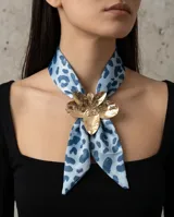 Pañuelo de seda celeste con estampado animal print azul y un dije metálico dorado en forma de flor que sujeta la prenda.