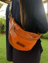 Riñonera de cuero vacuno color camel, con cierre principal y tirador de cuero, correa regulable y parche con logo grabado en el frente.