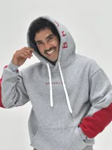Canguro gris con capucha, de corte holgado, con detalles en color rojo en las mangas y estampado de texto en color rojo en la capucha y el pecho.