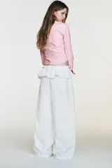 Pantalón blanco de nylon, tiro alto, con cintura elástica y detalle de sobrefalda o peplum superpuesto con hebilla metálica. Corte ancho y pierna recta.