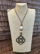 Colgante con dije de nudo celta en metal color bronce, unido a una serie de cuentas de piedra y resina en tonos tierra, beige y blanco, montado sobre un cordón de cuero marrón.