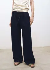 Jeans de corte wide leg en color azul oscuro, con tiro medio, cierre frontal de cremallera y botón, bolsillos laterales y detalle de pinzas en la cintura.