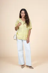 Blusa de algodón color amarillo pastel, con escote redondo ajustable mediante lazo, mangas cortas abullonadas con volados y diseño con textura delicada y terminaciones festoneadas.