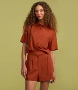 Short corto de mujer confeccionado en mezcla de lino y viscosa, color tostado. Presenta un diseño con pliegues delanteros, bolsillos laterales y un cierre asimétrico.