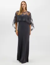 Vestido largo de corte sirena en color azul marino, confeccionado en tejido de punto con caída fluida. Presenta una capa integrada de tul fino sobre los hombros y espalda, decorada con bordados florales a tono y lentejuelas brillantes. Posee escote redondo y cierre invisible en la espalda.
