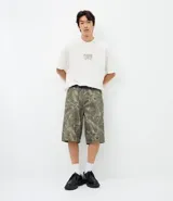 Bermuda de corte baggy confeccionada en sarga de algodón con estampado camuflado. Presenta cintura con trabillas, cierre frontal tradicional y bolsillos funcionales en la parte delantera y trasera.
