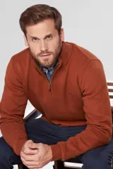 Buzo de lana color terracota con cuello alto y cierre frontal parcial. Presenta puños y ruedo acanalados, con detalle de logo bordado en el pecho y tirador de cierre en cuero.