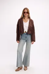 Chaqueta de efecto gamuza en color marrón, con solapas amplias, cierre frontal con botón y flecos largos decorativos en la parte frontal y trasera. Presenta un diseño estructurado de estilo western.