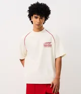 Remera oversized de color blanco marfil con detalles en rojo, cuello redondo, mangas cortas y grandes estampas tipográficas y gráficas en la espalda.