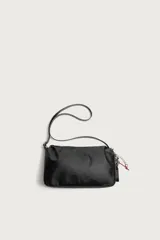 Bolso tipo bandolera de color negro, con compartimento principal con cierre de cremallera y bolsillo interior. Presenta un asa de hombro ajustable y un detalle decorativo de charms colgantes en uno de los laterales.