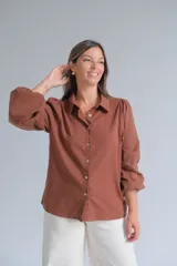 Camisa de color marrón chocolate, con cuello clásico, cierre frontal de botones y mangas largas abullonadas con detalle de tejido calado en los puños.