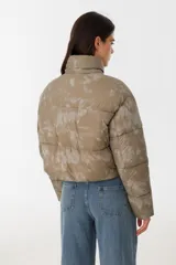 Campera puffer corta color verde con estampado difuminado, cierre frontal con cremallera, cuello alto y bolsillos con solapa y hebilla.