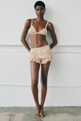 Shorts satinados color beige, con tiro medio, cintura elástica y diseño fluido. Presentan bordados florales en los laterales y volantes con puntillas en el bajo.