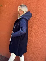 Montgomery de corte largo con capucha, confeccionado en una combinación de tejido de textura tipo bouclé en el cuerpo y mangas de nylon acolchado al tono. Presenta cierre frontal con botones tipo toggles y bolsillos laterales amplios.