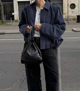 Chaqueta tipo bomber de calce holgado y silueta relajada, confeccionada en gamuza color azul marino. Presenta cuello camisero, cierre frontal oculto y mangas amplias con puños rectos.