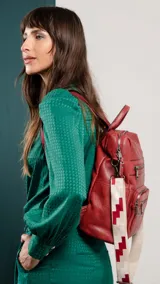 Mochila de símil cuero color marrón con apertura superior y tres bolsillos frontales con cierres metálicos. Cuenta con bolsillos laterales y una correa de galón con diseño geométrico, regulable y extraíble, que permite su uso como bandolera.