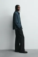 Camisa de corte relajado confeccionada en tejido fluido con mezcla de viscosa. Presenta cuello italiano, manga larga con puños abotonados y cierre frontal con botonadura, destacando por el detalle de jaretas verticales a ambos lados de la tapeta.
