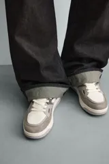 Zapatilla deportiva de cordones, con parte superior en combinación de piezas y materiales en tonos blanco, gris claro y gris oscuro. Suela con volumen.