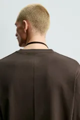 Camiseta de manga larga con corte relajado, confeccionada en tejido de algodón compacto. Presenta cuello redondo y detalle de costura en el centro de la espalda.