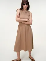 Vestido midi de algodón color tostado, sin mangas, con escote bote y cuerpo elastizado con frunces tipo smock. Presenta falda fluida de corte recto.