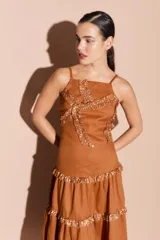 Top color marrón con tirantes finos y escote cuadrado. Presenta detalles de volados y lentejuelas doradas en el frente.