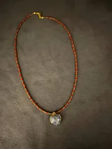 Collar corto de piedras semipreciosas facetadas grises y doradas, con un dije colgante en forma de corazón de piedra natural enmarcado en metal dorado.