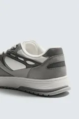 Zapatilla deportiva de cordones, con parte superior en combinación de piezas y materiales en tonos blanco, gris claro y gris oscuro. Suela con volumen.
