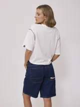 Remera blanca de algodón con corte cropped y calce holgado. Tiene cuello redondo con ribete azul y logo de la marca estampado en el pecho.