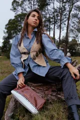 Top de cuero en color beige con diseño estructurado, cuenta con correas ajustables con hebillas metálicas y apliques decorativos de escudos metálicos en el frente.