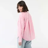 Camisa de manga larga confeccionada en popelina de algodón, con diseño de rayas verticales en tonos rosa y blanco. Presenta cuello clásico, cierre frontal con botones y corte holgado.
