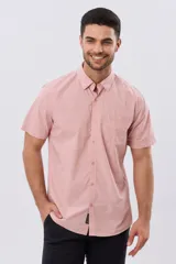 Camisa lisa de manga corta en color rosado, con calce slim, cuello camisero, cierre frontal con botones y un bolsillo aplicado en el pecho.