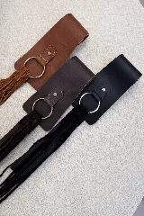 Faja de diseño estructurado en color negro, confeccionada en una combinación de napa lisa y gamuza. Presenta un cierre frontal con argolla metálica plateada y detalle de flecos laterales largos.