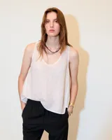 Top sin mangas de lino color blanco, con escote redondo, corte A y fit relajado. Presenta ruedo más corto en el delantero que en la espalda y recortes laterales. Tiene lavado fade teñido en frío que genera un efecto melange.