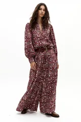 Pantalón de lino color bordó con estampado floral de margaritas en blanco, azul y naranja. Diseño de pierna ancha, tiro medio-alto con tablas delanteras, elástico en la parte trasera y bolsillos laterales.