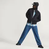 Pantalón de denim azul de corte holgado, tiro medio y diseño clásico con las tres tiras características de Adidas a lo largo de los laterales.