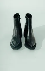 Bota corta de cuero negro, con caña media y punta cuadrada. Se caracteriza por su taco geométrico y voluminoso, con acabado texturado.