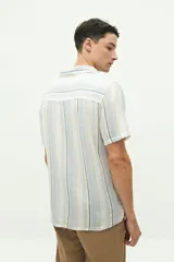 Camisa de manga corta con cuello cubano, confeccionada en una mezcla de lino y algodón con textura. Presenta un diseño a rayas verticales en tonos beige y celeste sobre fondo blanco, con cierre frontal de botones y logo bordado en el pecho.