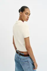 Top de punto color blanco marfil con cuello polo y manga corta. Presenta detalle de puntilla con forma de onda en el cuello y los puños.