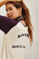 Remera estilo beisbolera con mangas raglán en color violeta oscuro y cuerpo en tono crema. Presenta una estampa frontal con texto en color negro.