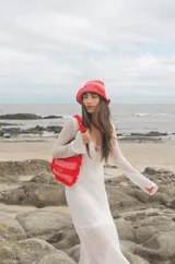 Cartera tipo shoulder bag tejida a crochet en hilo de algodón, con diseño a rayas en tonos de rojo y rosado, y detalles de volados en los bordes y la manija de hombro.