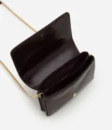 Cartera bandolera pequeña de poliuretano color marrón oscuro con acabado texturizado. Cuenta con solapa frontal, logo metálico dorado en la parte inferior y correa larga de cadena metálica dorada.
