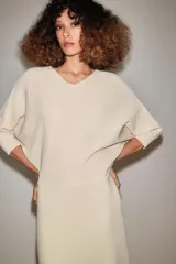 Vestido midi de punto color marfil con escote en V, mangas largas de sisa ancha, cintura entallada y falda de corte evasé.
