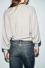 Chaqueta de punto color beige claro, de cuello redondo y manga larga abullonada con puño ajustado. Cierre frontal cruzado con botones plateados.