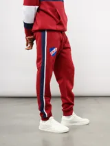 Pantalon de jogging azul de felpa, con franjas laterales en blanco y azul marino. Presenta el escudo del Club Nacional de Football en el muslo derecho y el logo de Umbro en el izquierdo.