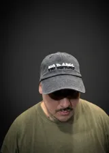 Gorro tipo dad hat de color gris oscuro con efecto gastado, visera estructurada y ajustador trasero regulable. Cuenta con bordado frontal con el texto "No Basic" en dos tonos contrastantes.