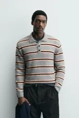 Polo de punto de corte relajado con diseño de rayas horizontales en tonos gris, rosa y marrón. Presenta cuello solapa, cierre frontal con botonadura y mangas largas con puños acanalados.