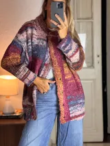 Saco tejido de punto con diseño multicolor en tonos rojizos, amarillos y azules. Presenta un corte holgado, cierre frontal con botones y textura rugosa.
